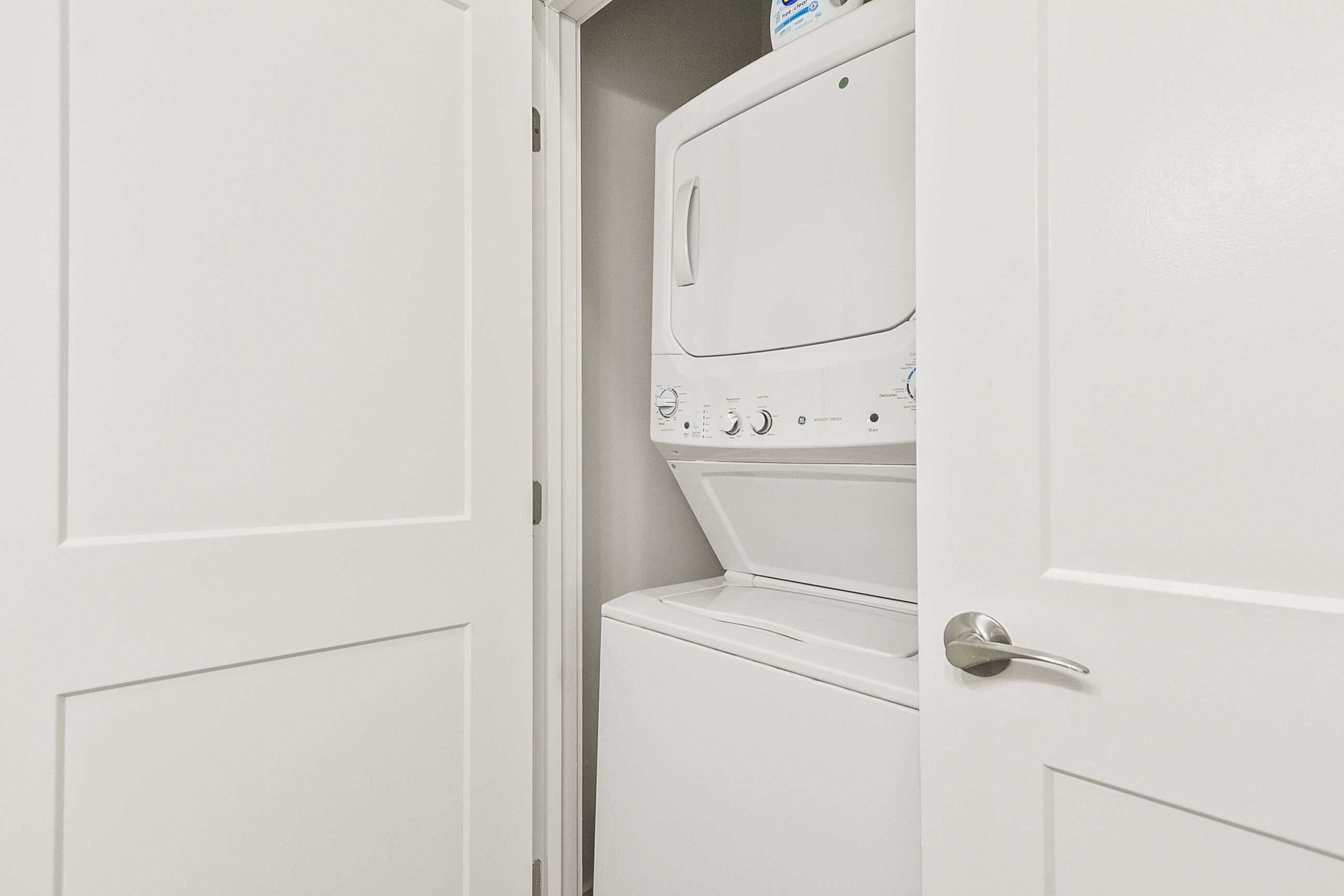 A laundry room with a front-loading washer and dryer, a door with a silver handle, and a white door frame.