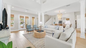 A spacious living room with a large sofa, a coffee table, and a television. There is a staircase leading to another level, and a chandelier hangs from the ceiling. - Southern Breeze Family Home 2 Pools Private Beach (Gulf Shores)
