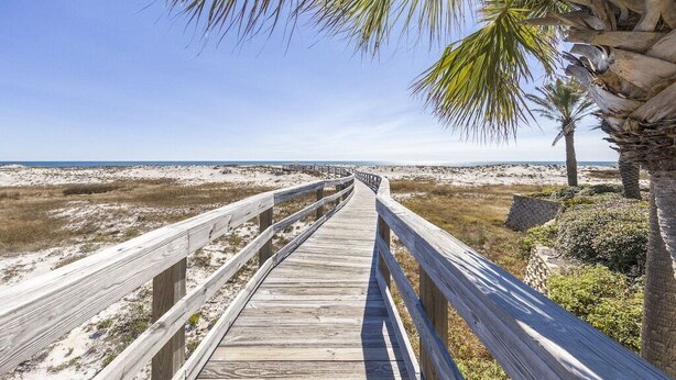 A wooden boardwalk leading to a beach with sand dunes and palm trees. - Southern Breeze Family Home 2 Pools Private Beach (Gulf Shores)