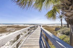A wooden boardwalk leading to a beach with sand dunes and palm trees. - Southern Breeze Family Home 2 Pools Private Beach (Gulf Shores)