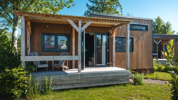 A wooden cabin with a covered porch, sliding glass doors, and two chairs outside. - Group Accommodation for 40 Guests (Scherpenzeel)