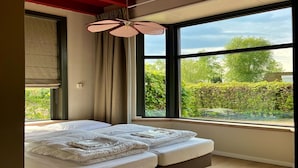 A modern bedroom with a large bed, a ceiling fan, and a view of greenery outside. - Group Accommodation for 40 Guests (Scherpenzeel)