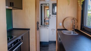 A compact kitchen with a built-in oven, a sink, and a window with a view of greenery. - Group Accommodation for 40 Guests (Scherpenzeel)