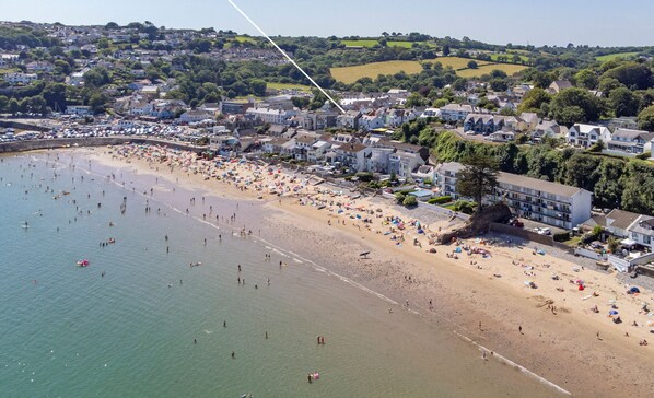 Un pueblo costero con una playa de arena, numerosos sombrillas de playa y un edificio con la inscripción "The Old Cottage".