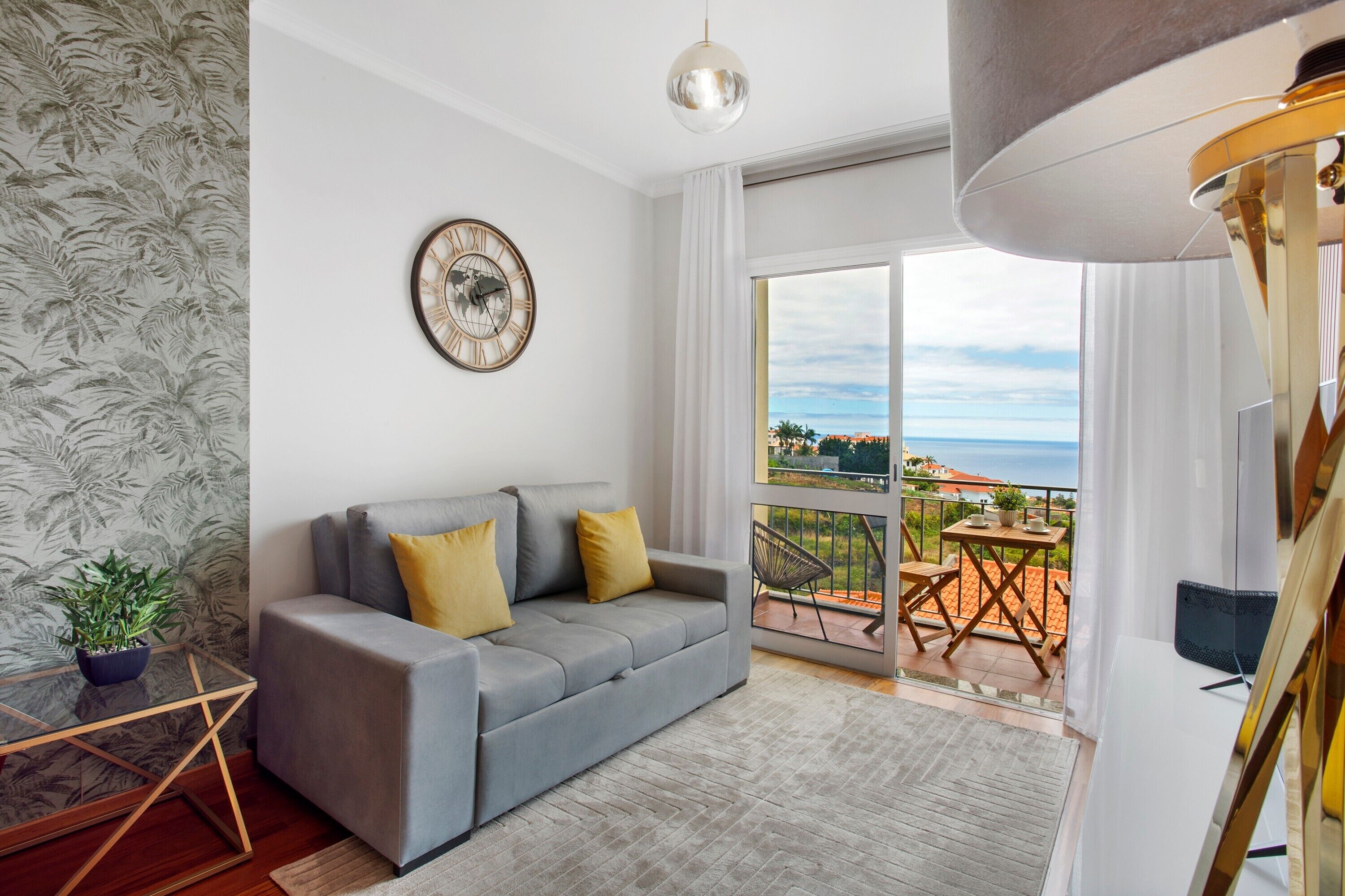 Uma sala de estar moderna com um sofá cinzento, um relógio de parede e uma varanda com vista.