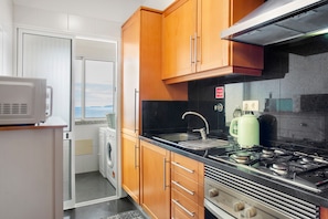 A compact kitchen with wooden cabinets, a stainless steel stove, a microwave, and a washing machine.