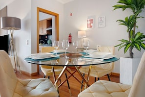 A dining area with a glass table, cushioned chairs, and a kitchen in the background.