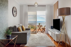 A modern living room with a sofa, TV, and balcony with a view.