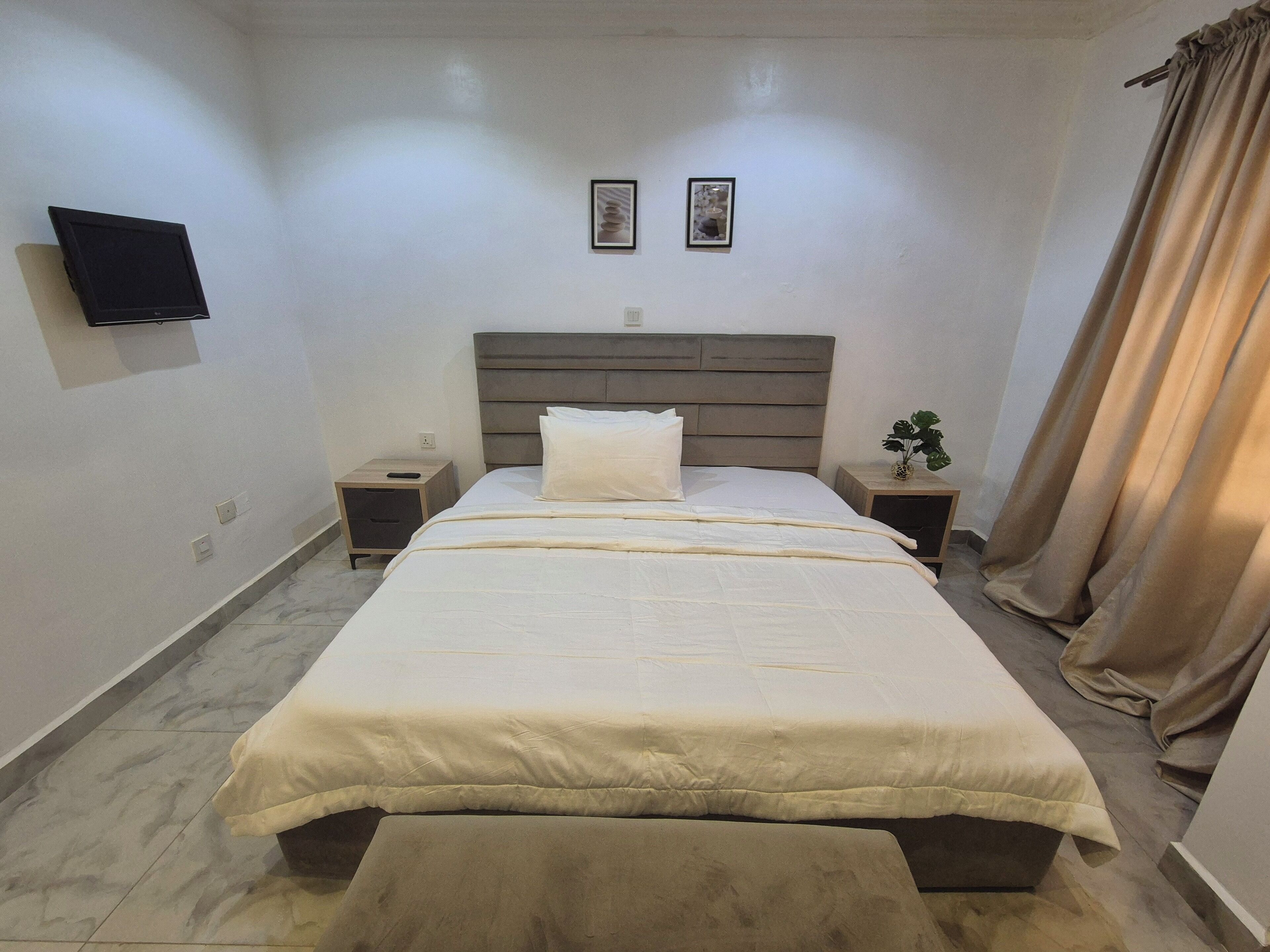 A neatly made bed with a headboard, a bedside table with a lamp, and a wall-mounted TV.