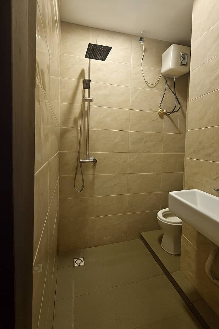 Un baño pequeño con azulejos, ducha, inodoro y lavamanos.
