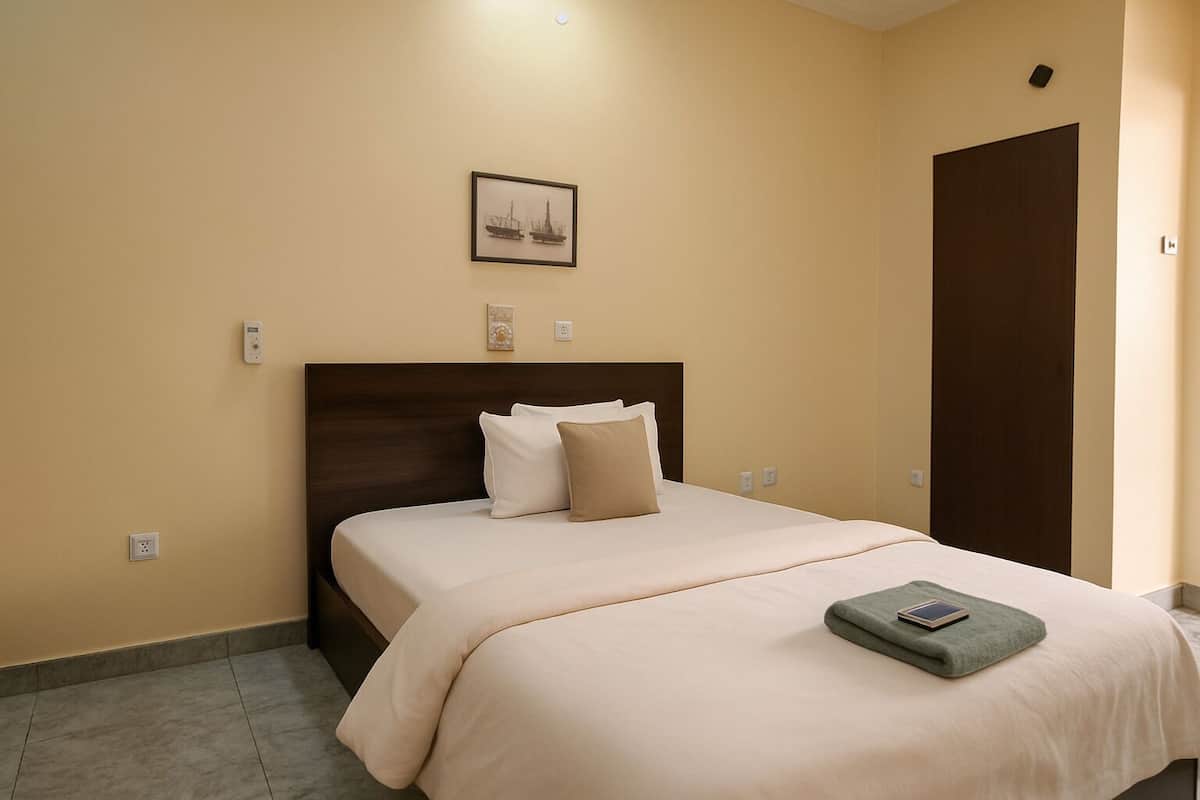A hotel room with a bed, a headboard, a nightstand, a bedside table, a phone, and a wall-mounted picture.