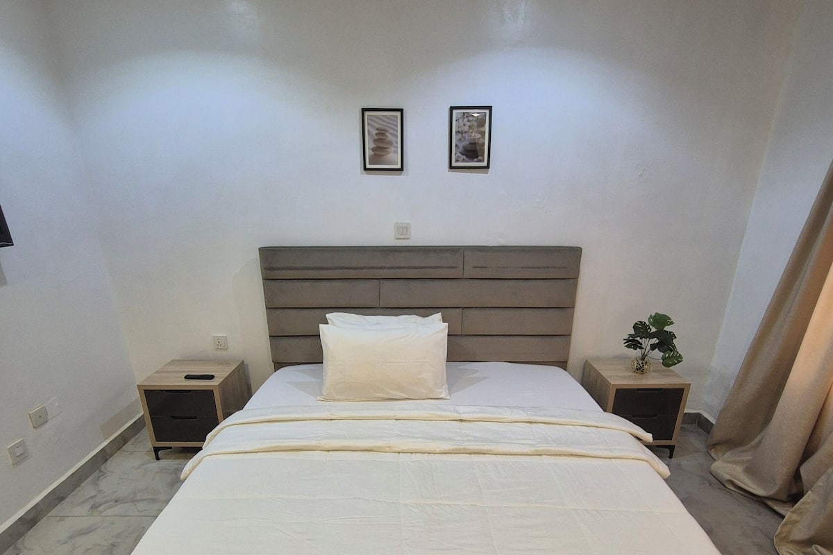 A bedroom with a large bed, two bedside tables, a headboard, and two framed pictures on the wall.