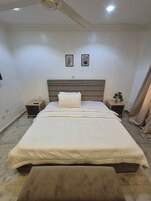 Un dormitorio con una cama grande, dos mesitas de noche, un cabecero y dos cuadros enmarcados en la pared.