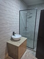 Un baño moderno con tocador de mármol, cabina de ducha de vidrio y puerta de madera.