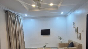 A living room with a beige sofa, a coffee table, a ceiling fan, and a flat-screen TV mounted on the wall. - Al-Ihsan Metro Hotel (Kaduna)