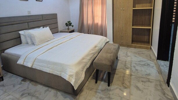 A bedroom with a bed, a bench, a wardrobe, and a ceiling fan. - Al-Ihsan Metro Hotel (Kaduna)