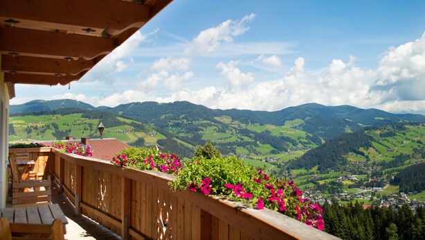 A wooden balcony with a view of green hills and a town in the distance. - Apartment 'Almrausch' with Shared Terrace, Balcony and Wi-Fi (Wagrain)