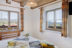 Un dormitorio con una cama, dos ventanas con cortinas, un cabecero de madera y vistas a un paisaje.