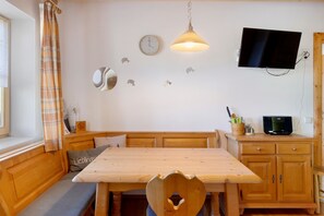 Una habitación acogedora con una mesa de madera, asientos tipo banco, un televisor y un reloj en la pared.