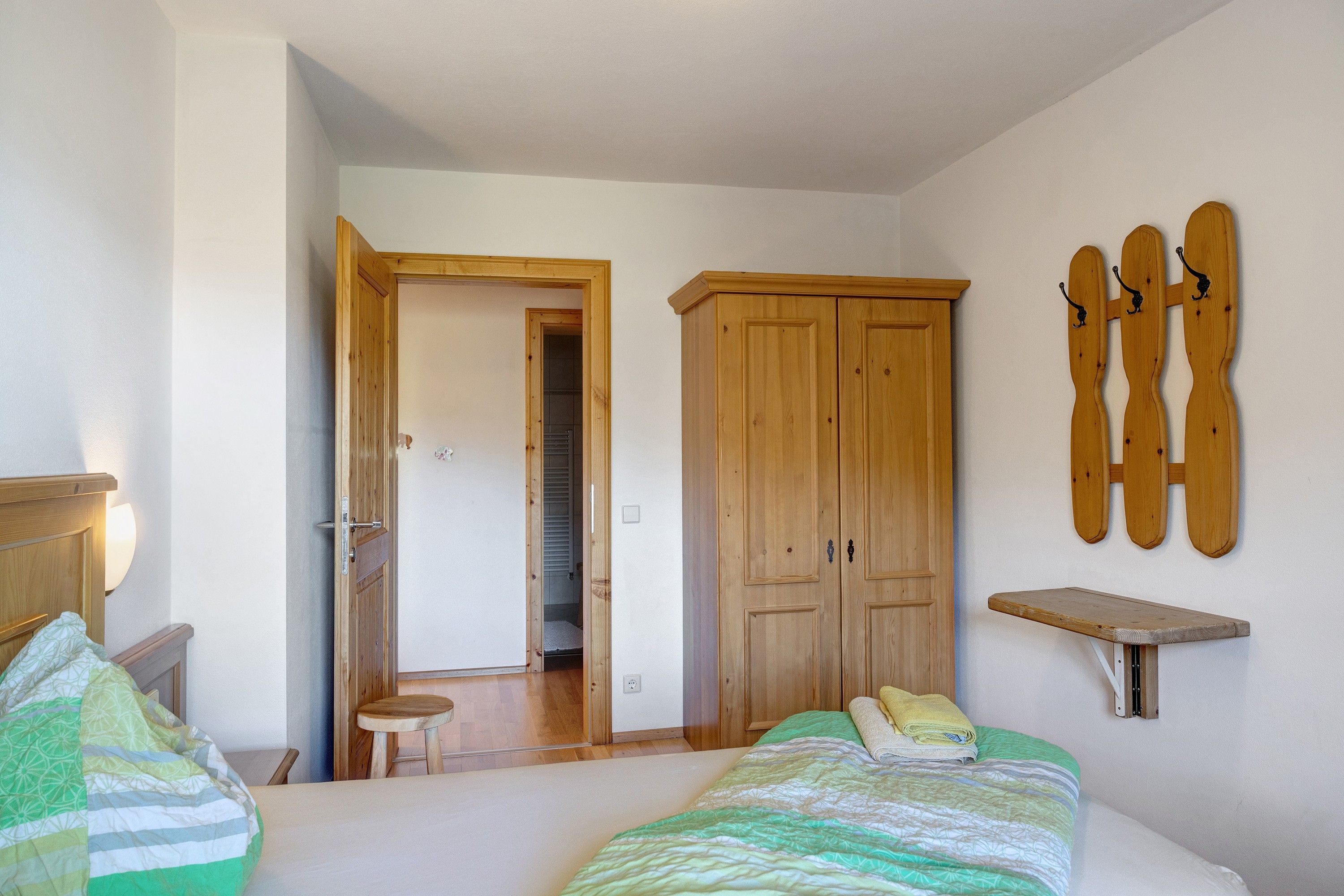 A bedroom with two beds, a wooden wardrobe, a wooden stool, and a wall-mounted shelf.