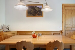 Una mesa de comedor de madera con un banco, dos lámparas colgantes, un cuadro enmarcado de un paisaje y un florero decorativo con forma de manzana.