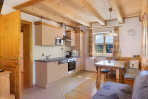 Een kleine keuken met houten kastjes, een magnetron, een fornuis en een raam met gordijnen.