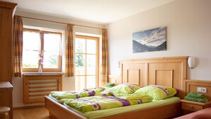Un dormitorio con una cama, una ventana con cortinas, un radiador, un cuadro en la pared y una mesita de noche con una lámpara.