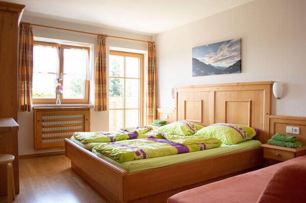 Ein Schlafzimmer mit Bett, einem Fenster mit Vorhängen, einem Heizkörper, einem Bild an der Wand und einem Nachttisch mit Lampe.