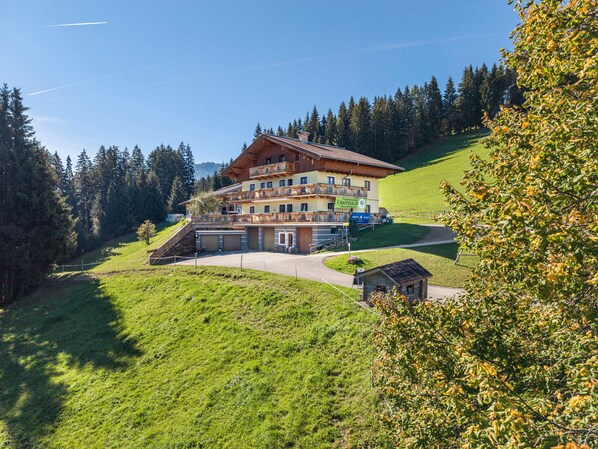 A multi-story hotel with a sloped roof, located on a hillside with a view of a forest.