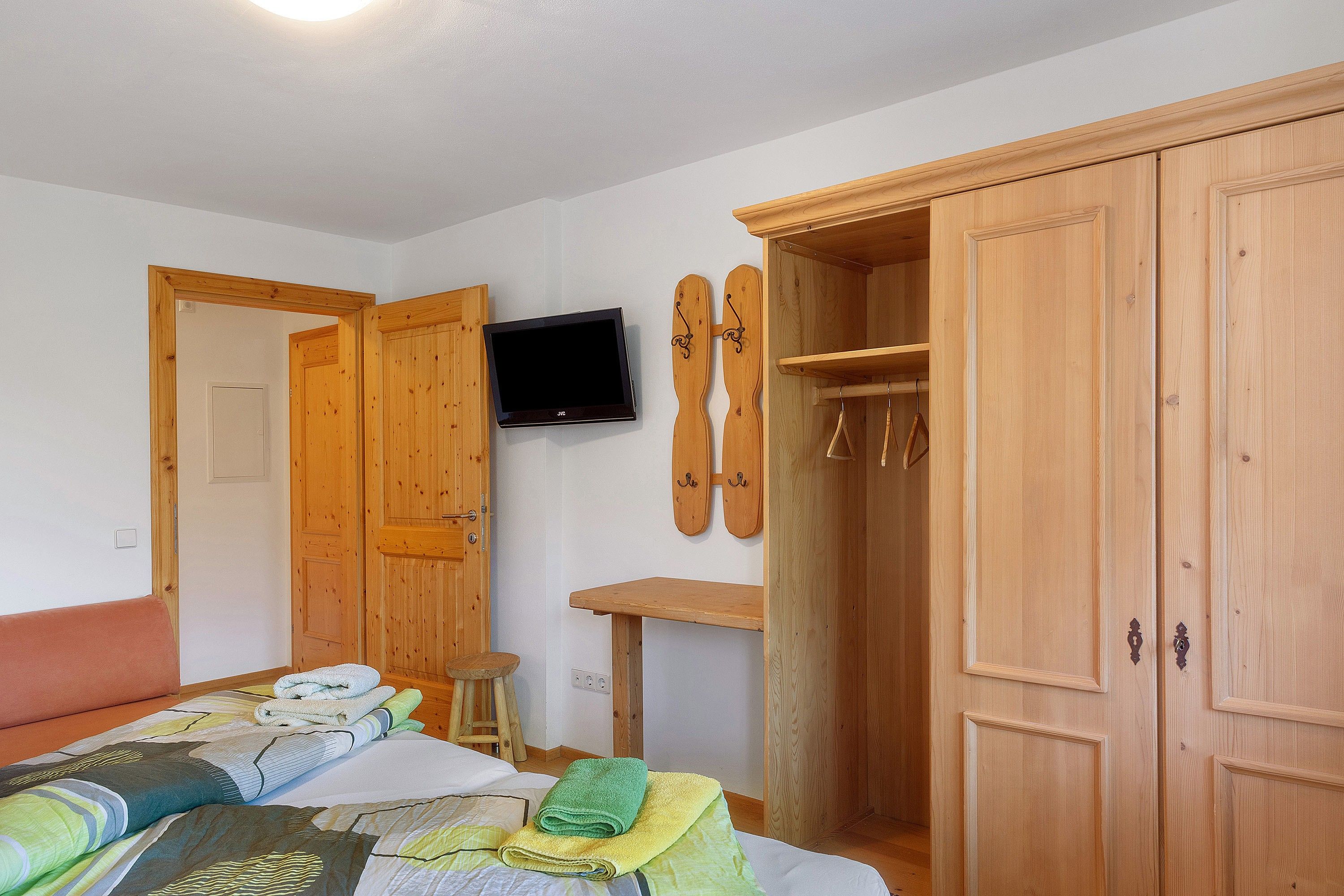 A bedroom with a bed, a wooden wardrobe, a television mounted on the wall, and a ski rack.