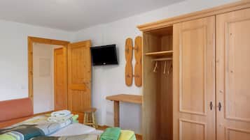 A bedroom with a bed, a wooden wardrobe, a television mounted on the wall, and a ski rack.