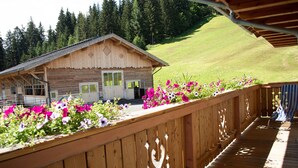 Una cabaña de madera con balcón, rodeada de una cerca de madera y flores coloridas.