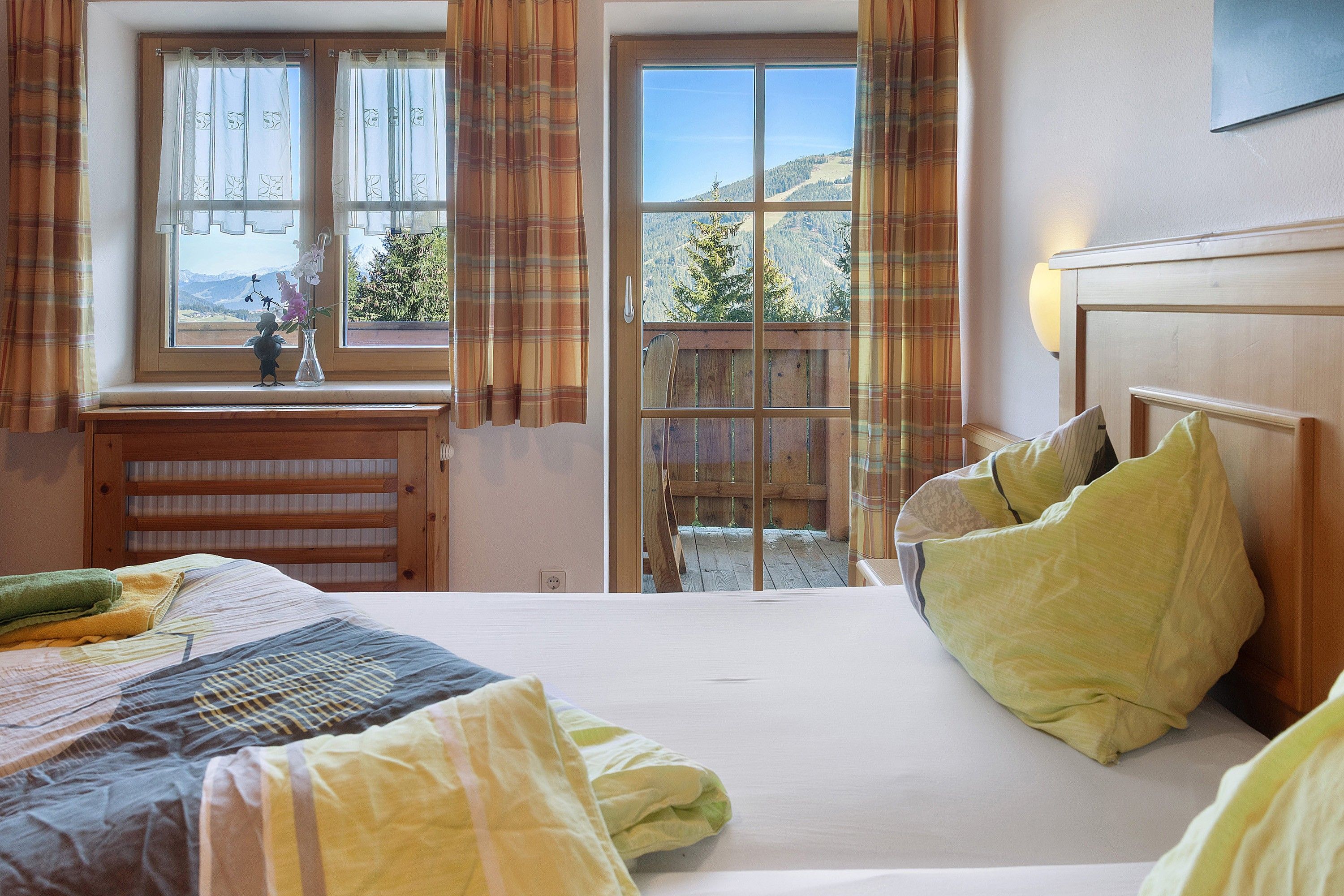 Ein Schlafzimmer mit einem Bett, einem Fenster mit Vorhängen, Blick ins Freie und einem Holzkopfende.