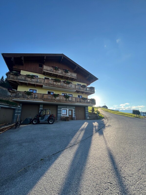 A multi-story building with balconies, a parked vehicle, and a gravel driveway.