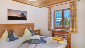 Un dormitorio con cabecera de madera, cama con varios almohadones, ventana con cortinas y un cuadro en la pared.