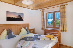 Ein Schlafzimmer mit Holz-Kopfteil, einem Bett mit vielen Kissen, einem Fenster mit Vorhängen und einem Gemälde an der Wand.