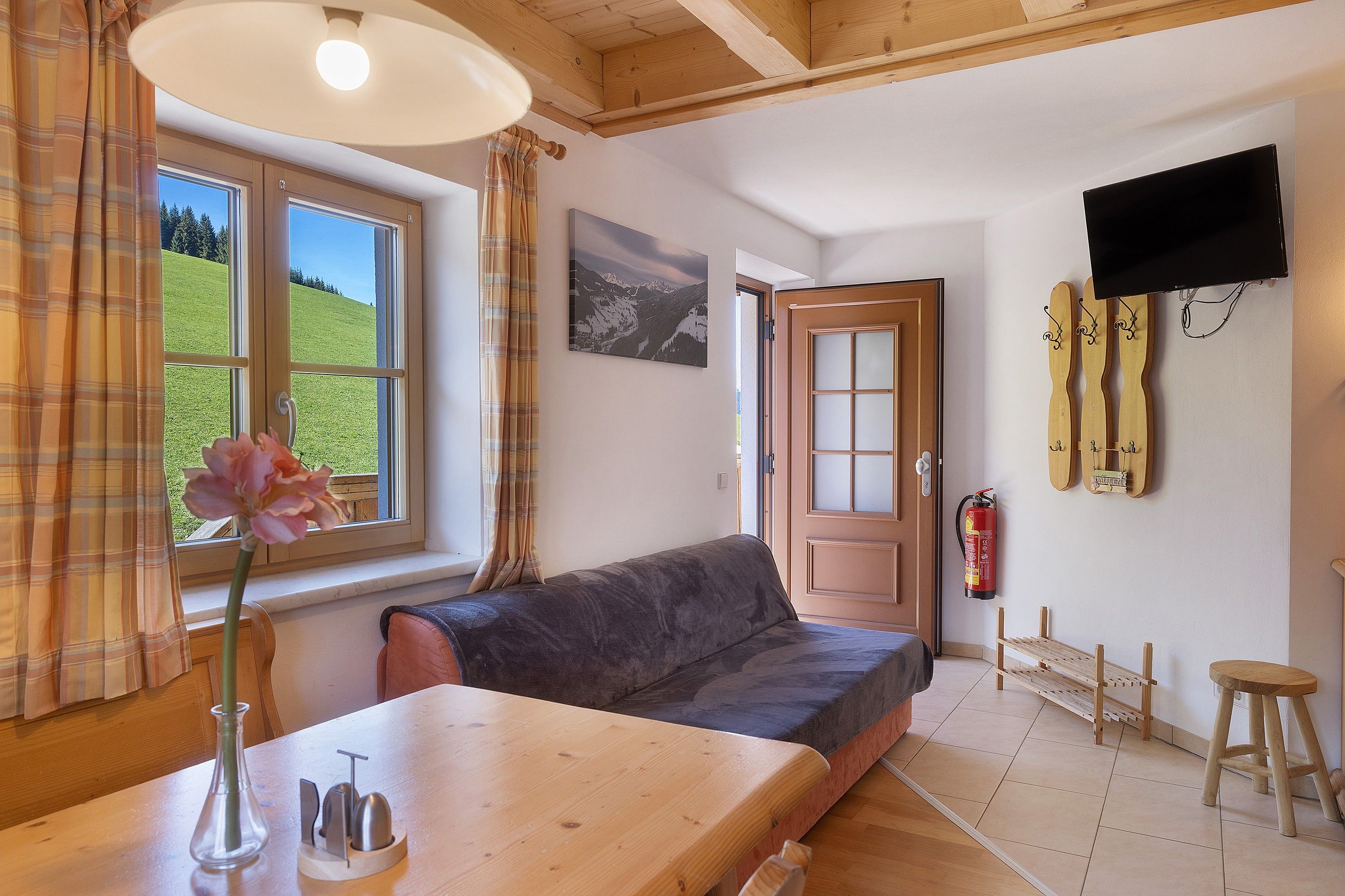 Una habitación acogedora con una mesa de madera, un sofá, una ventana con cortinas, un televisor montado y un extintor en la pared.