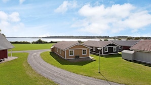 A row of single-story houses with a gravel driveway leading to a grassy area, a body of water in the background, and a clear sky.