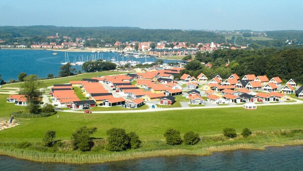 A coastal village with red-roofed houses, a marina, and a lake.