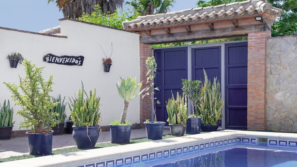 A pool area with a 'BIENVENIDOS' sign, potted plants, and a blue door.