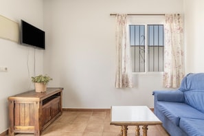 A living room with a TV, a sofa, a coffee table, and a window with curtains.