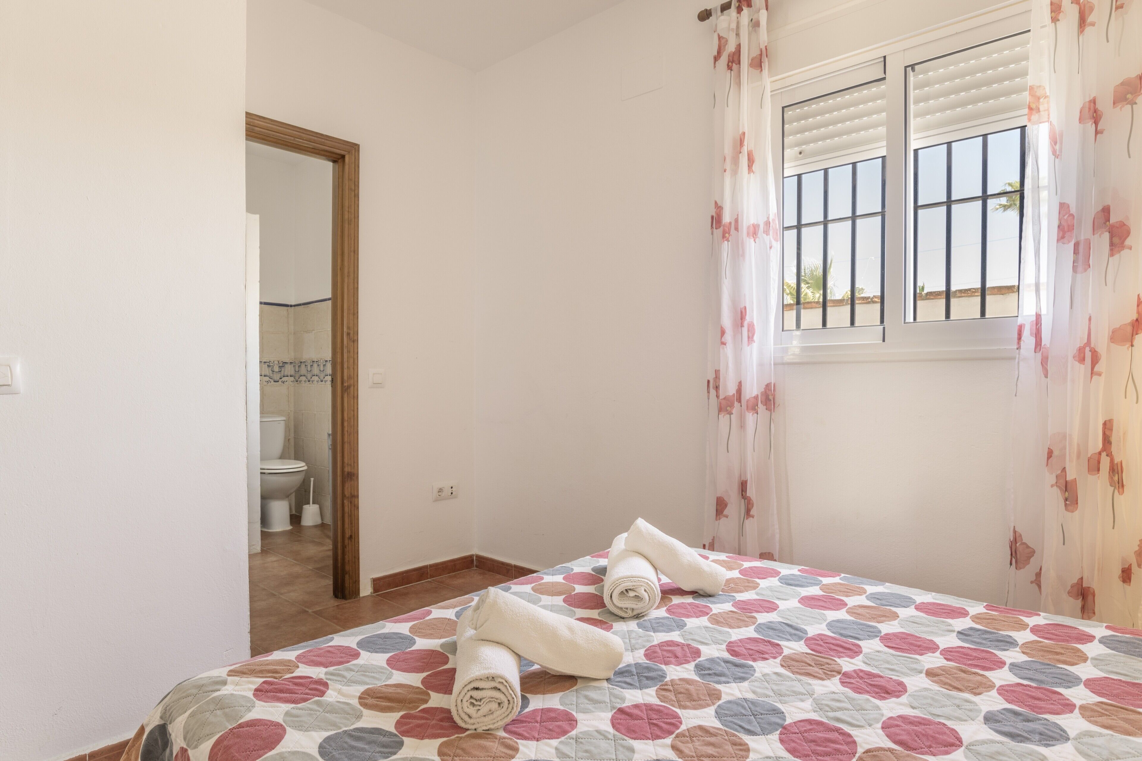 A bedroom with a bed, a window with curtains, and a view of a bathroom.