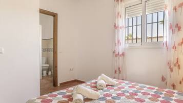 A bedroom with a bed, a window with curtains, and a view of a bathroom.