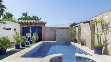 A swimming pool with a tiled edge, surrounded by potted plants and a stone wall.