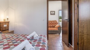 A hotel room with a bed, a wooden nightstand, a wall-mounted lamp, and a door leading to another room. - Apartment 'Elena 2' with Shared Pool and Private Terrace (Conil de la Frontera)