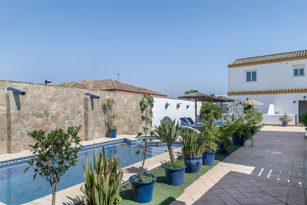 Un espace piscine agrémenté de murs en pierre, de plantes en pot et d’un bâtiment doté d’un toit en tuiles.