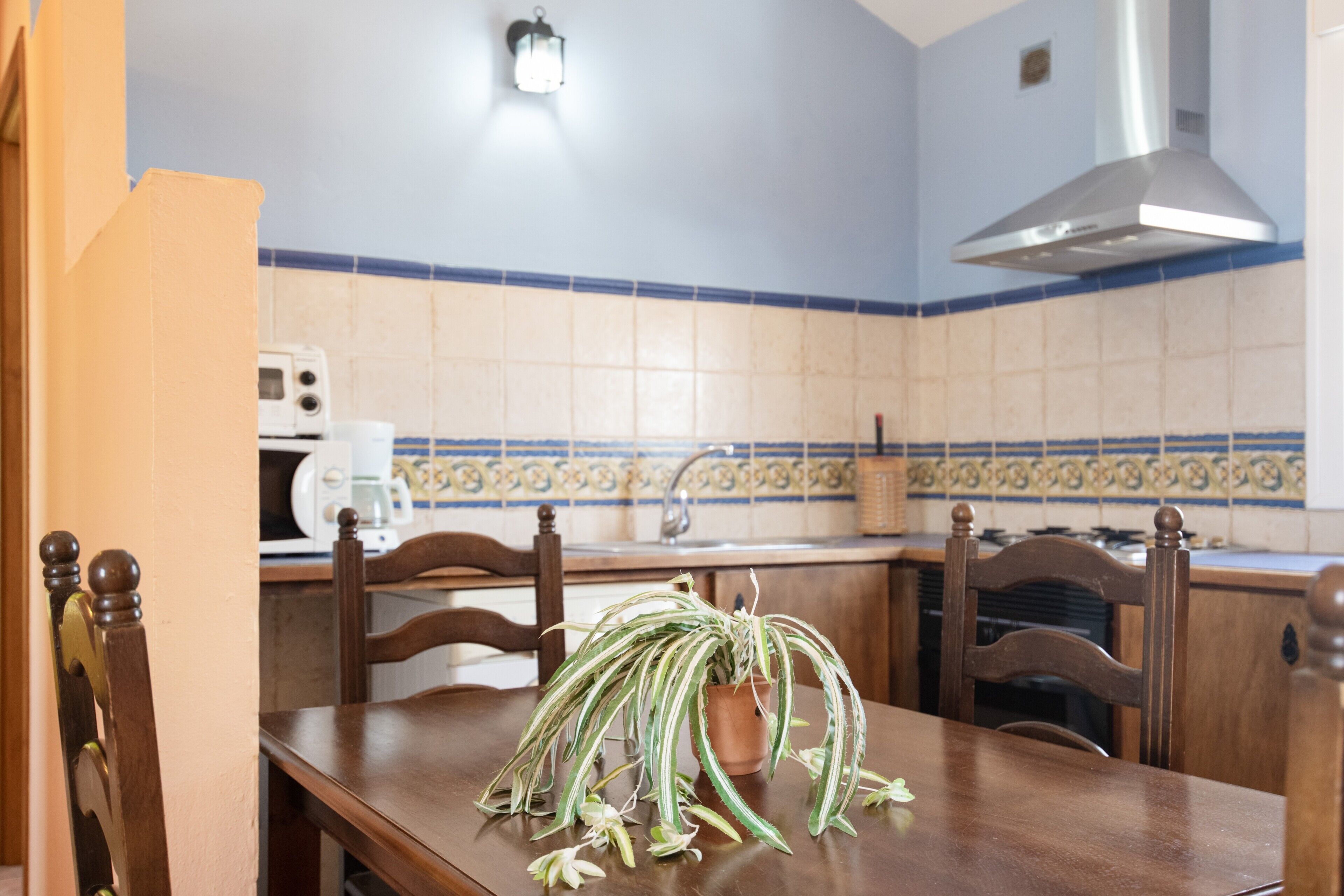 A kitchen with a dining table, chairs, a potted plant, a microwave, and a stove.