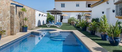 A swimming pool with lounge chairs, potted plants, and a white building with a tiled roof.