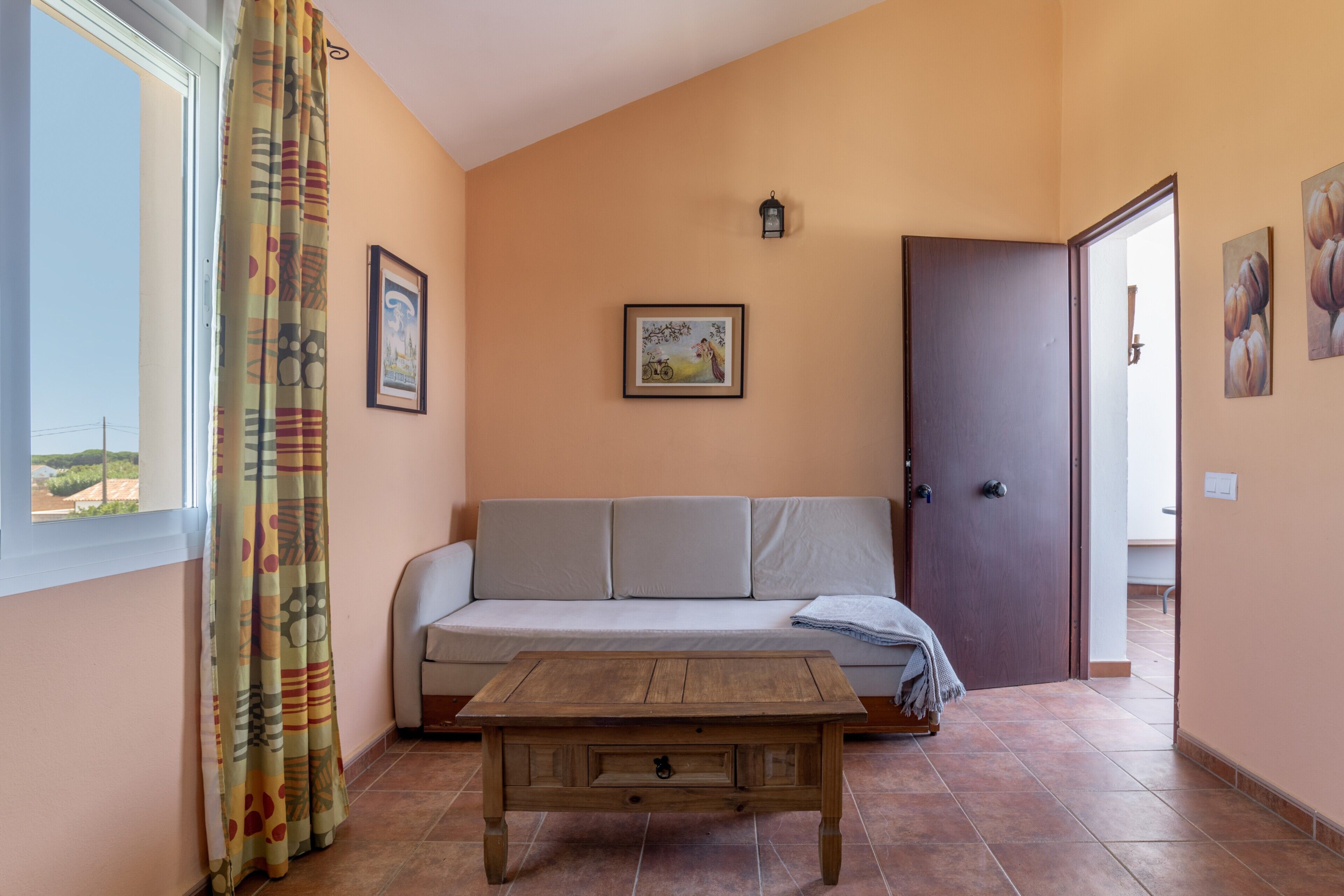 Una habitación con sofá, mesa de madera, puerta y ventana con cortinas.