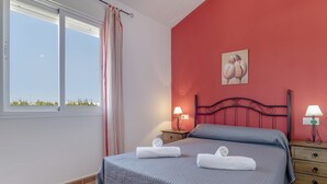 A bedroom with a bed, two bedside tables with lamps, a window with curtains, and a wall painting. - Apartment 'Fran' with Shared Pool and Terrace (Conil de la Frontera)